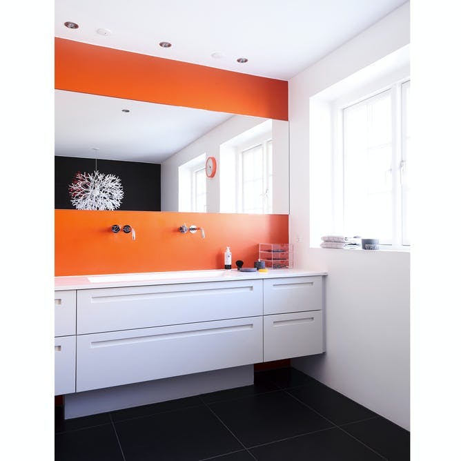 Badeværelse med pangfarver, orange vægge og lyse badeværelsesmøbler.