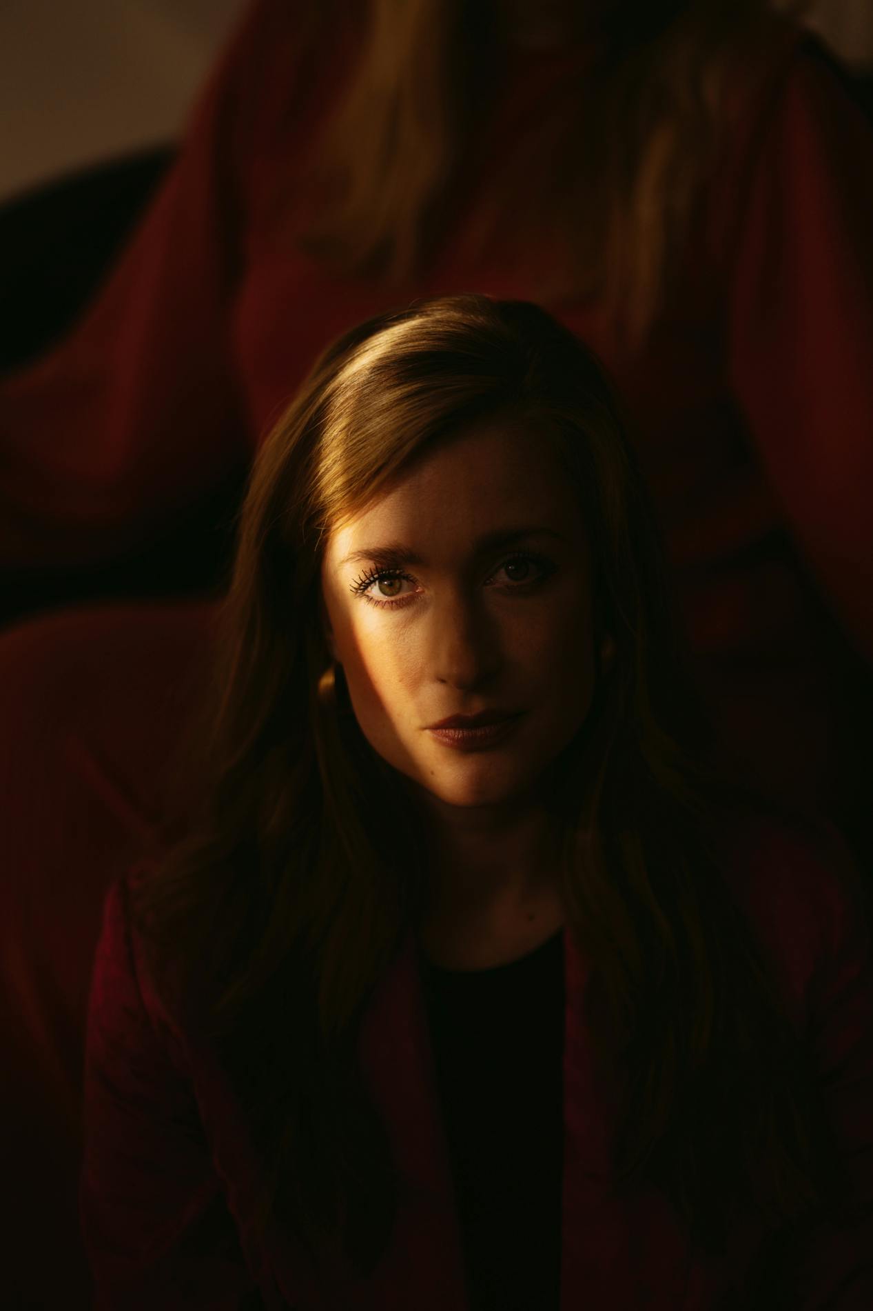 Camilla Søe fotograferet tæt på i et mørkt rum, der går en solstråle gennem hendes ansigt.