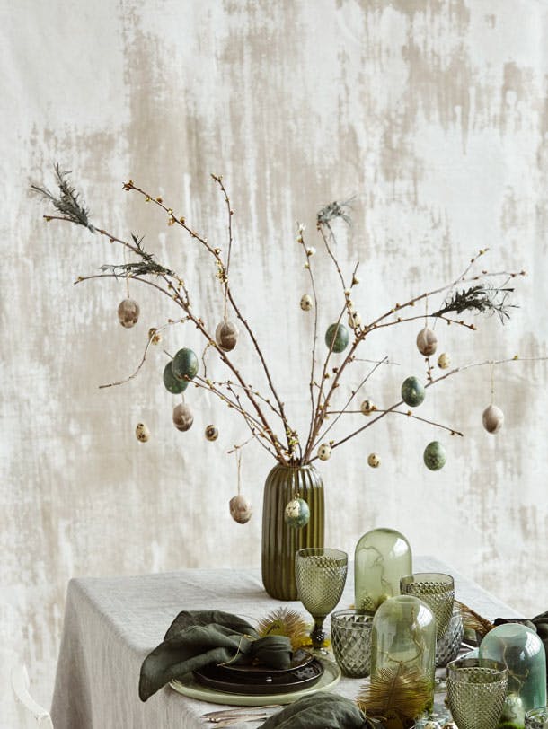 Vase med friske forårsgrene pyntet med påskeæg på påskebordet