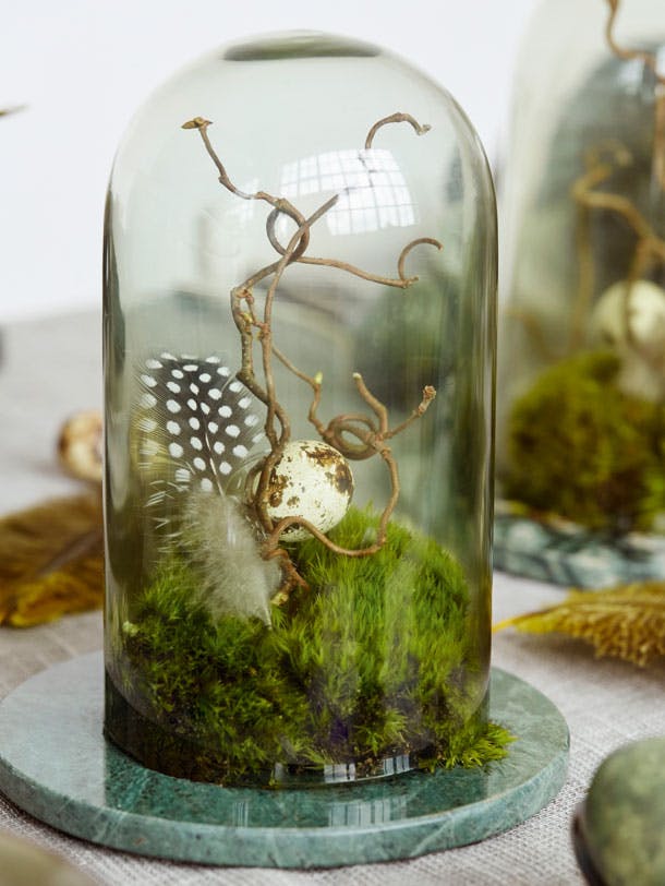 Kuppel med mos, påskeæg og fjer på påskebordet