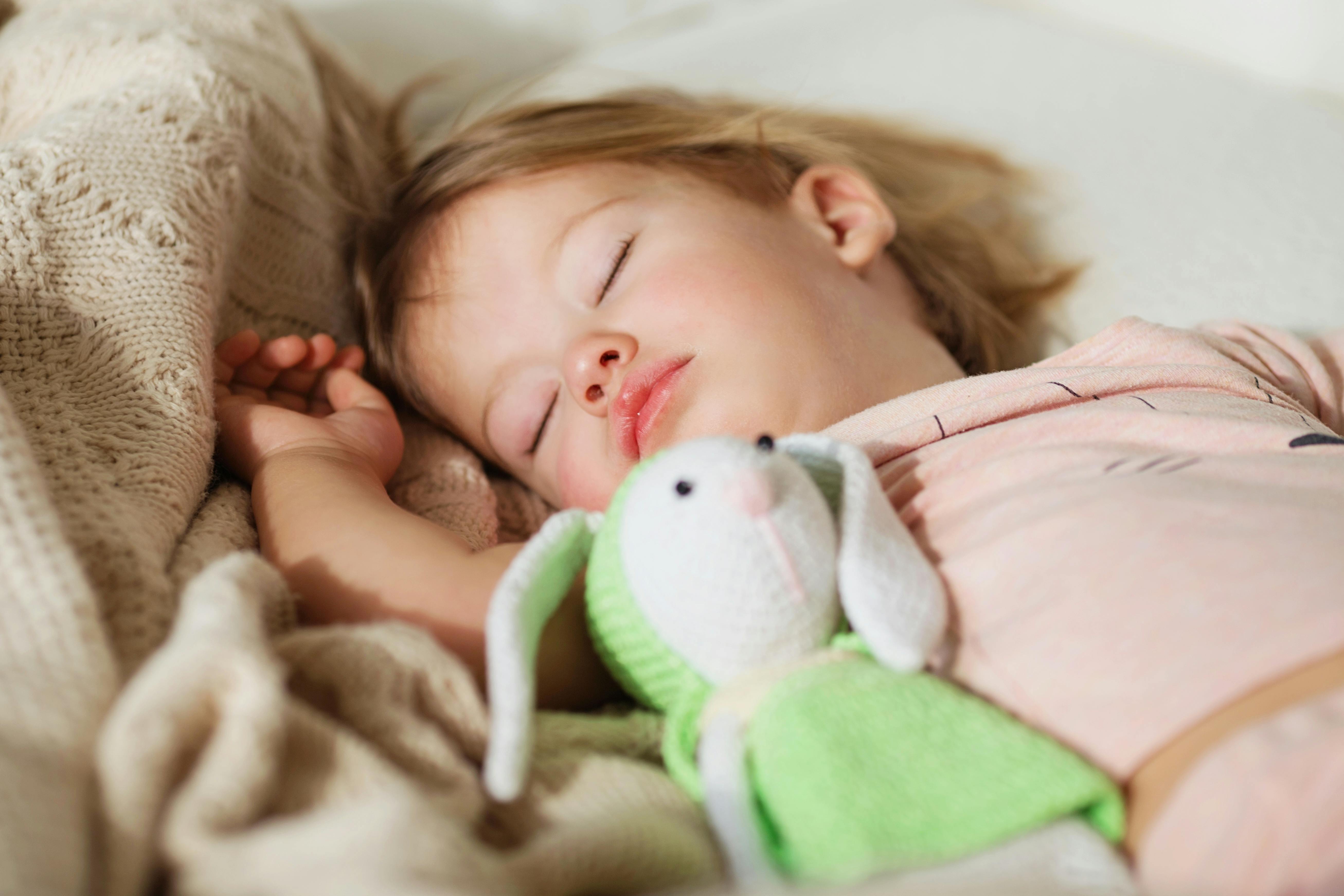 Sleeping little girl. Carefree sleep little baby with a soft toy on the bed. Close-up portrait of a beautiful sleeping child on knitted blanket. Sweet dreams