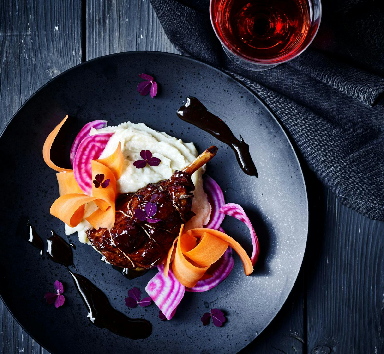 Braiserede spoleben og kartoffelmos med pastinak på sort service.