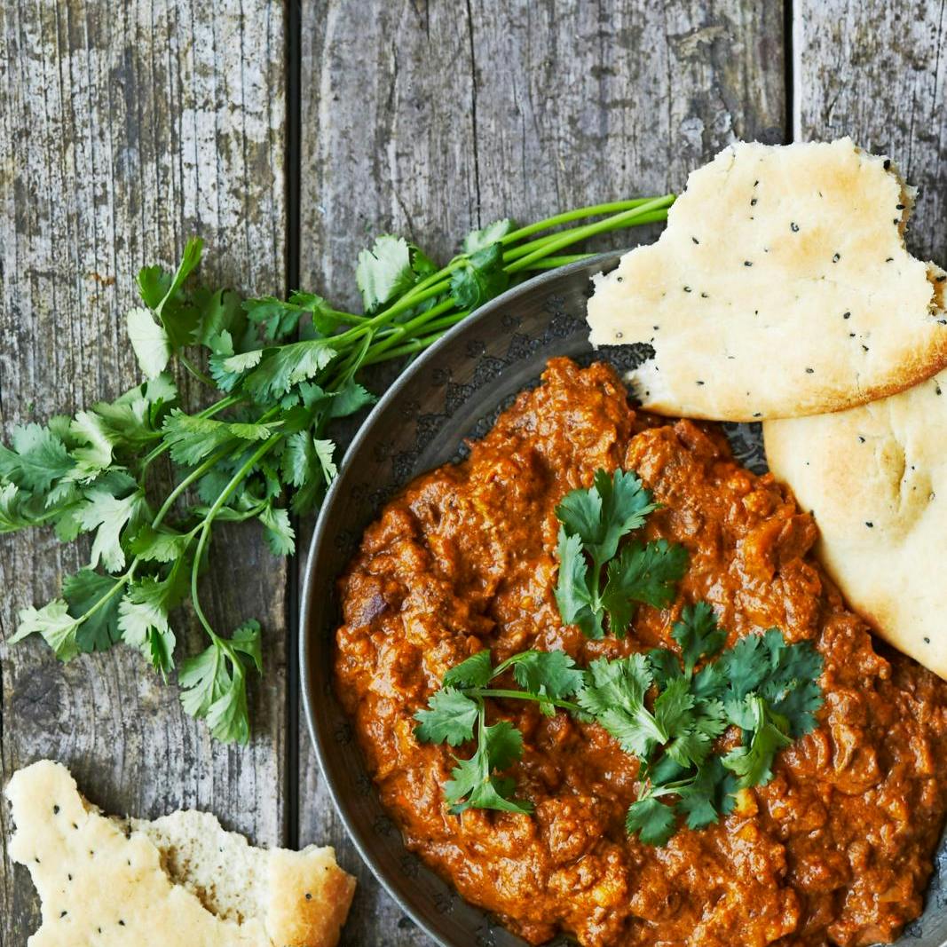 Indisk lammecurry på grå tallerken på rustikt plankebord.