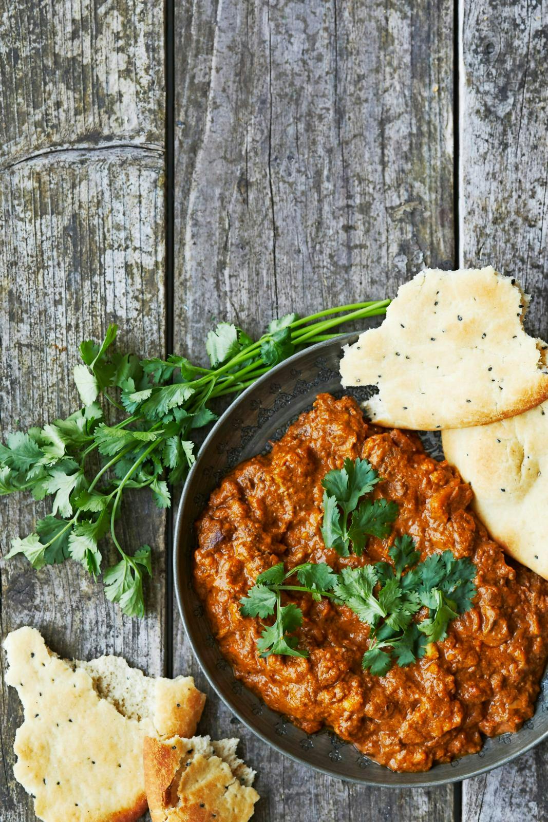 Indisk lammecurry på grå tallerken på rustikt plankebord.