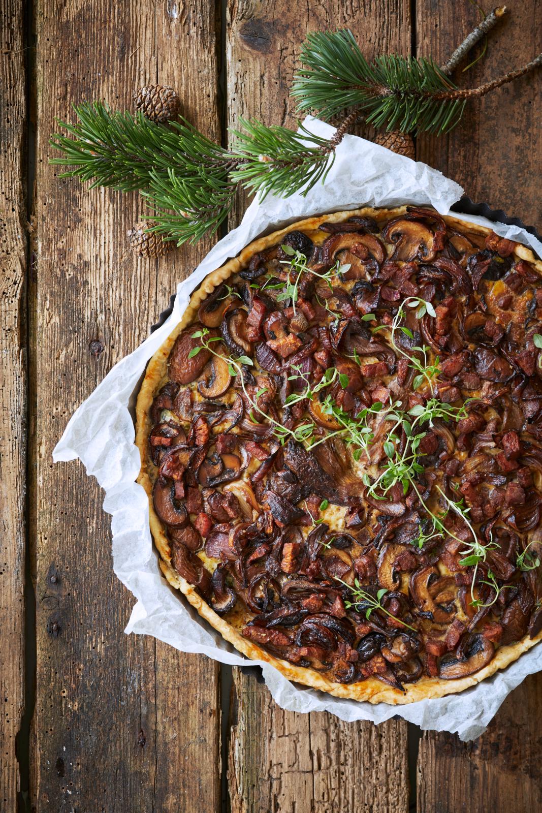 Svampetærte med karamelliserede løg og bacon serveret på rustik bordplade. 