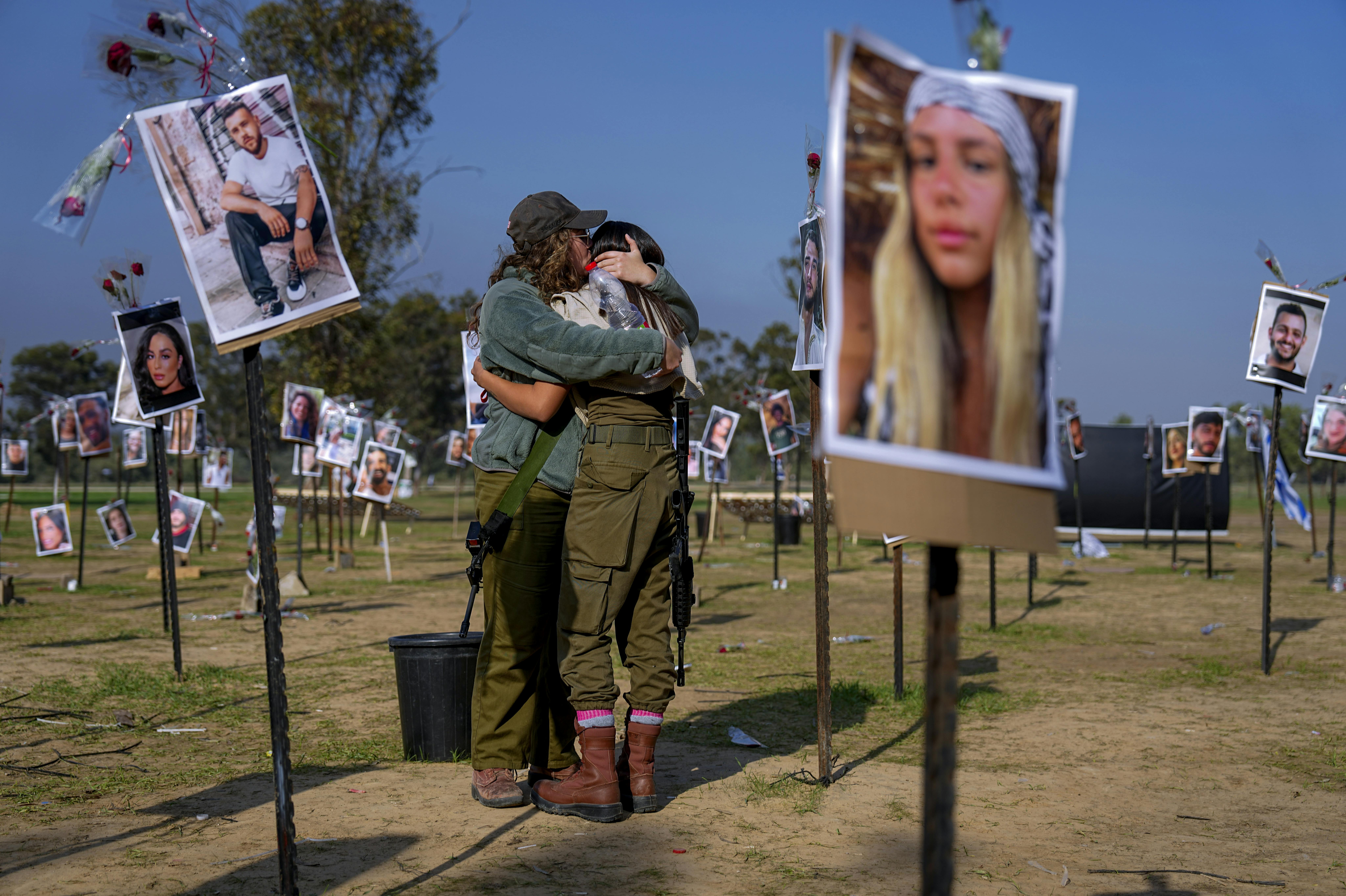 Israeli soldiers embrace next to photos of people killed and taken captive by Hamas militants during their violent rampage through the Nova music festival in southern Israel, which are displayed at the site of the event, to commemorate the October 7, massacre, near kibbutz Re'im, Friday, Dec. 1, 2023. (AP Photo/Ariel Schalit)