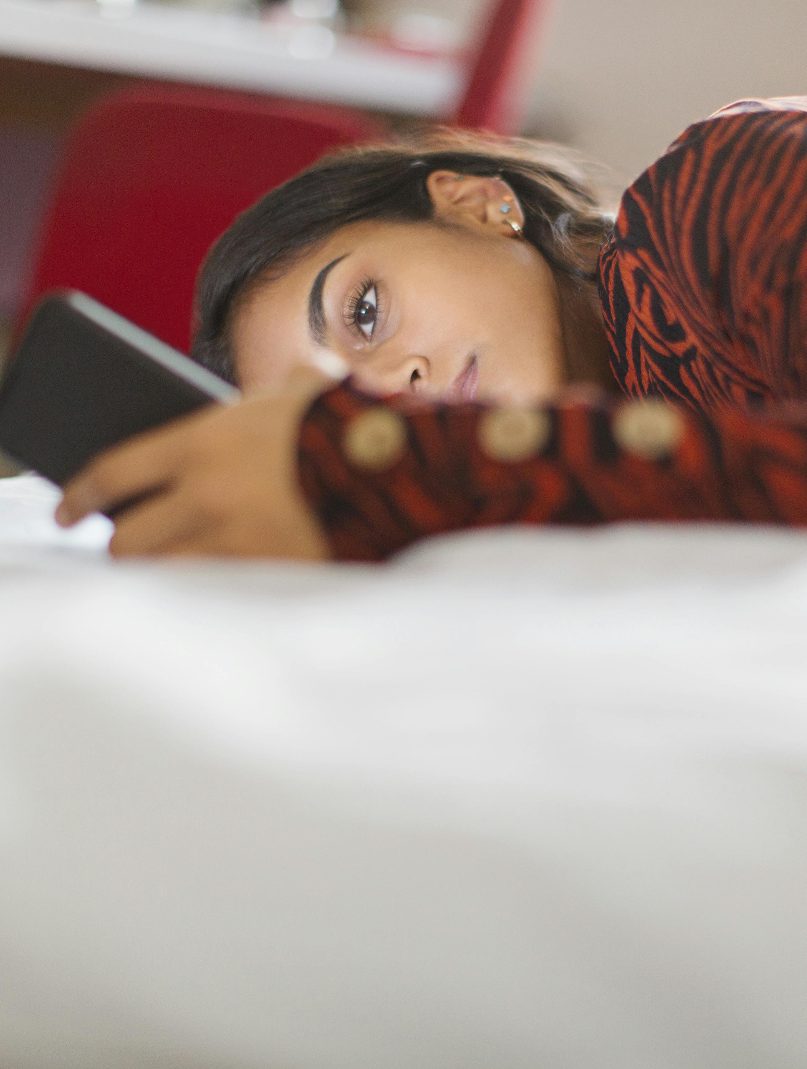 Focused teenage girl using smart phone laying on bed.