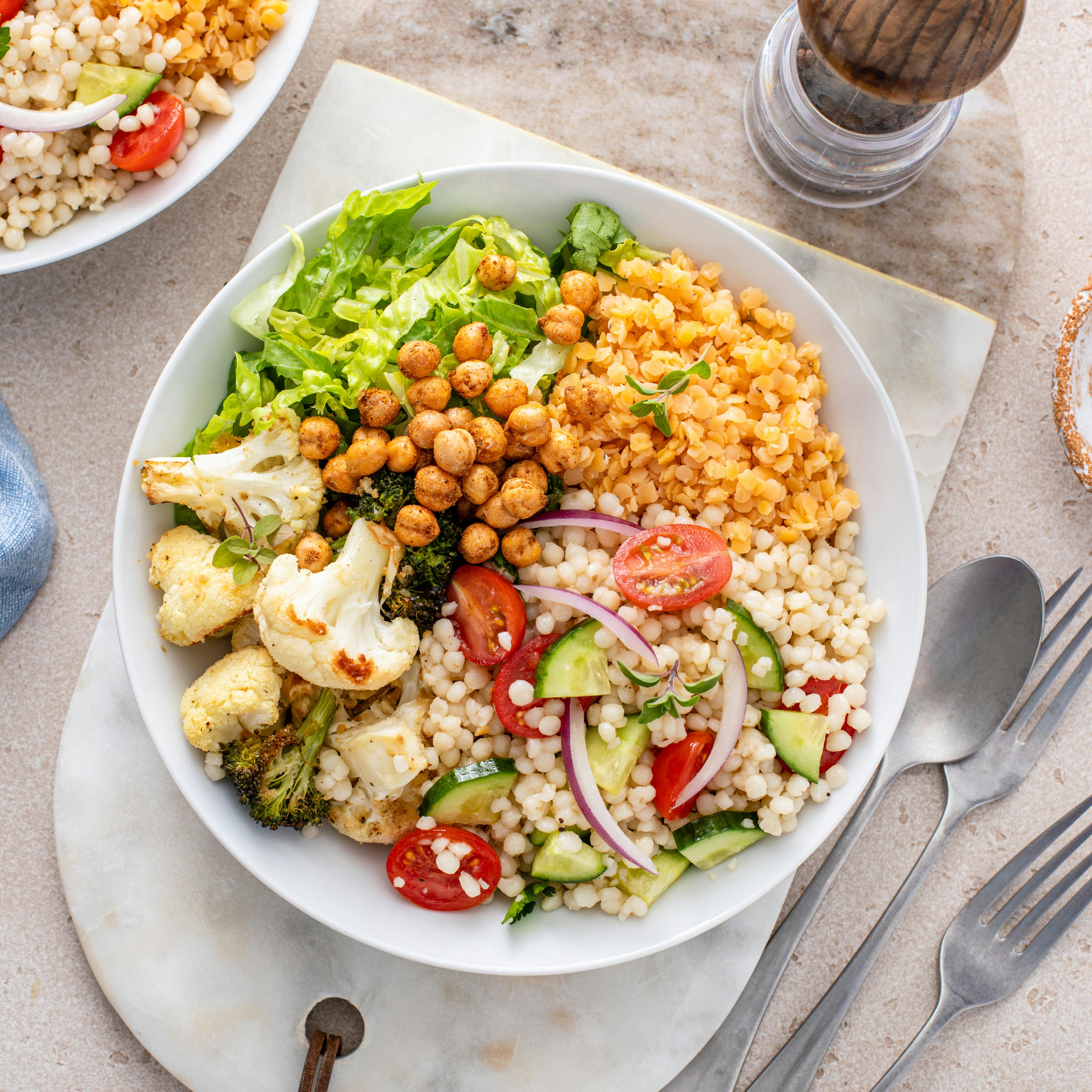 Vegan lunch bowl with roasted vegetables, fresh lettuce, cooked lentils, couscous salad and crunchy roasted chickpeas