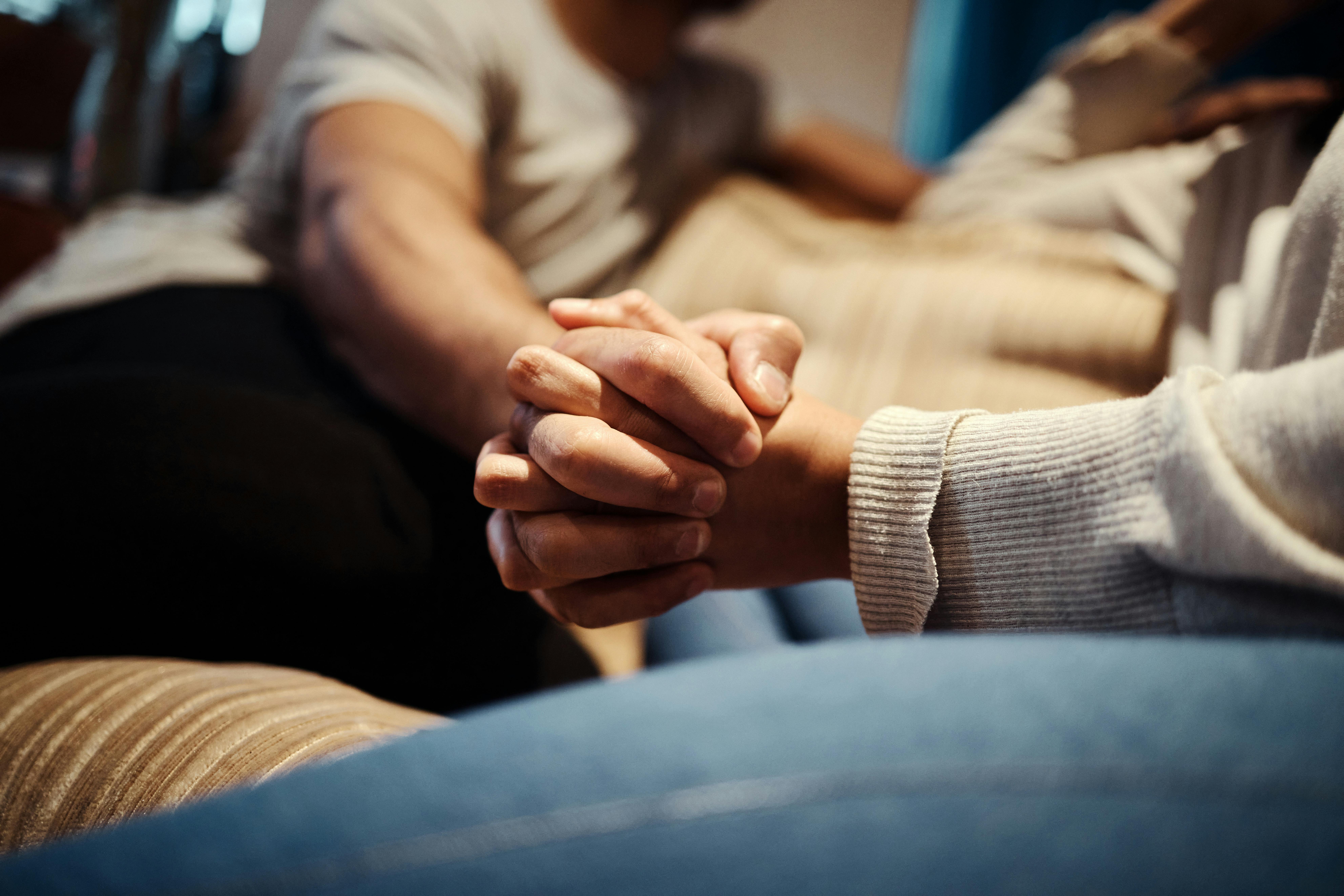 Holding hands, couple and love on couch for romance, home and support or empathy in marriage. People, trust and relax on sofa and connect on date in apartment, care and kindness in relationship.