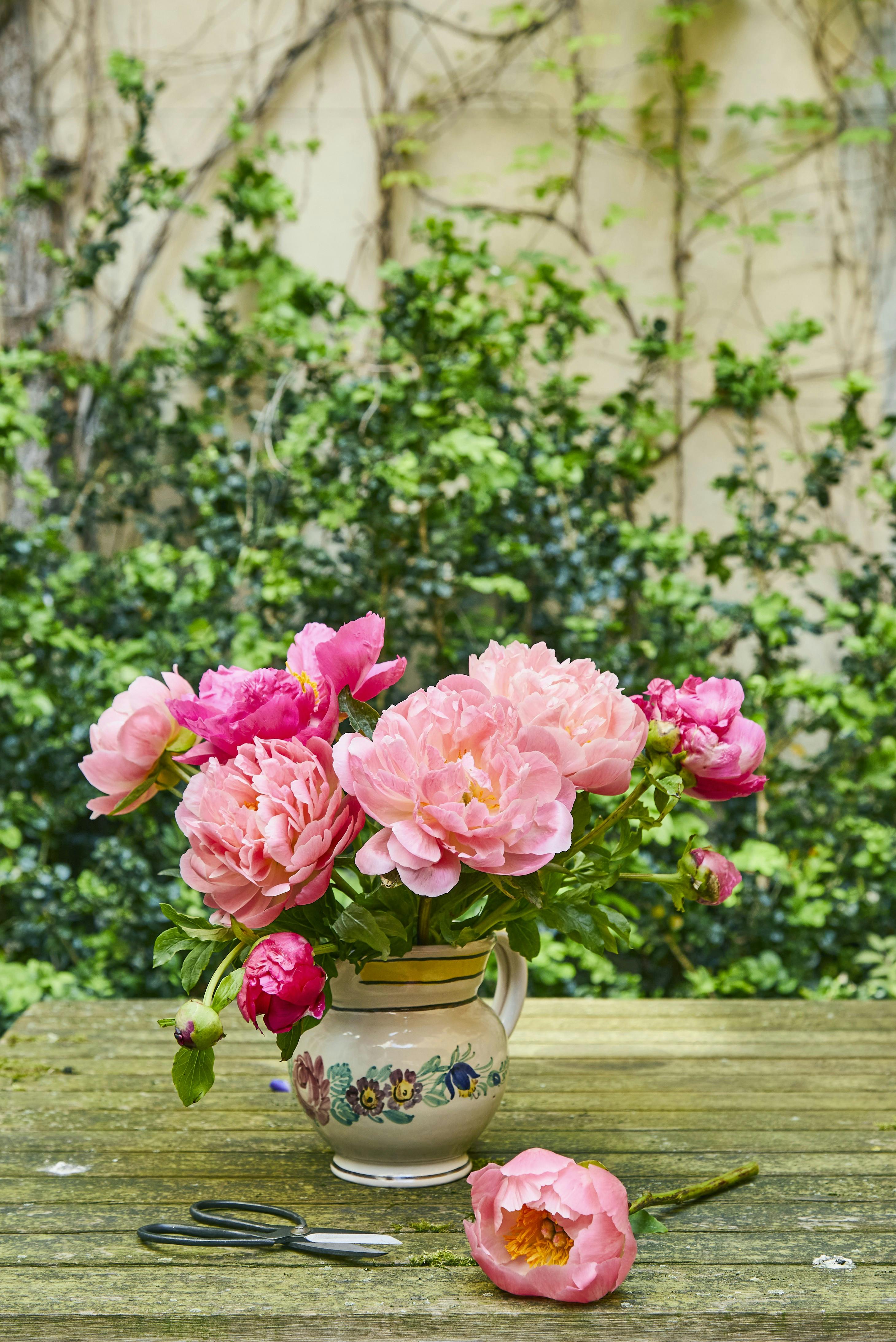 En håndfuld pink og koralrøde pæoner i en vintagekande