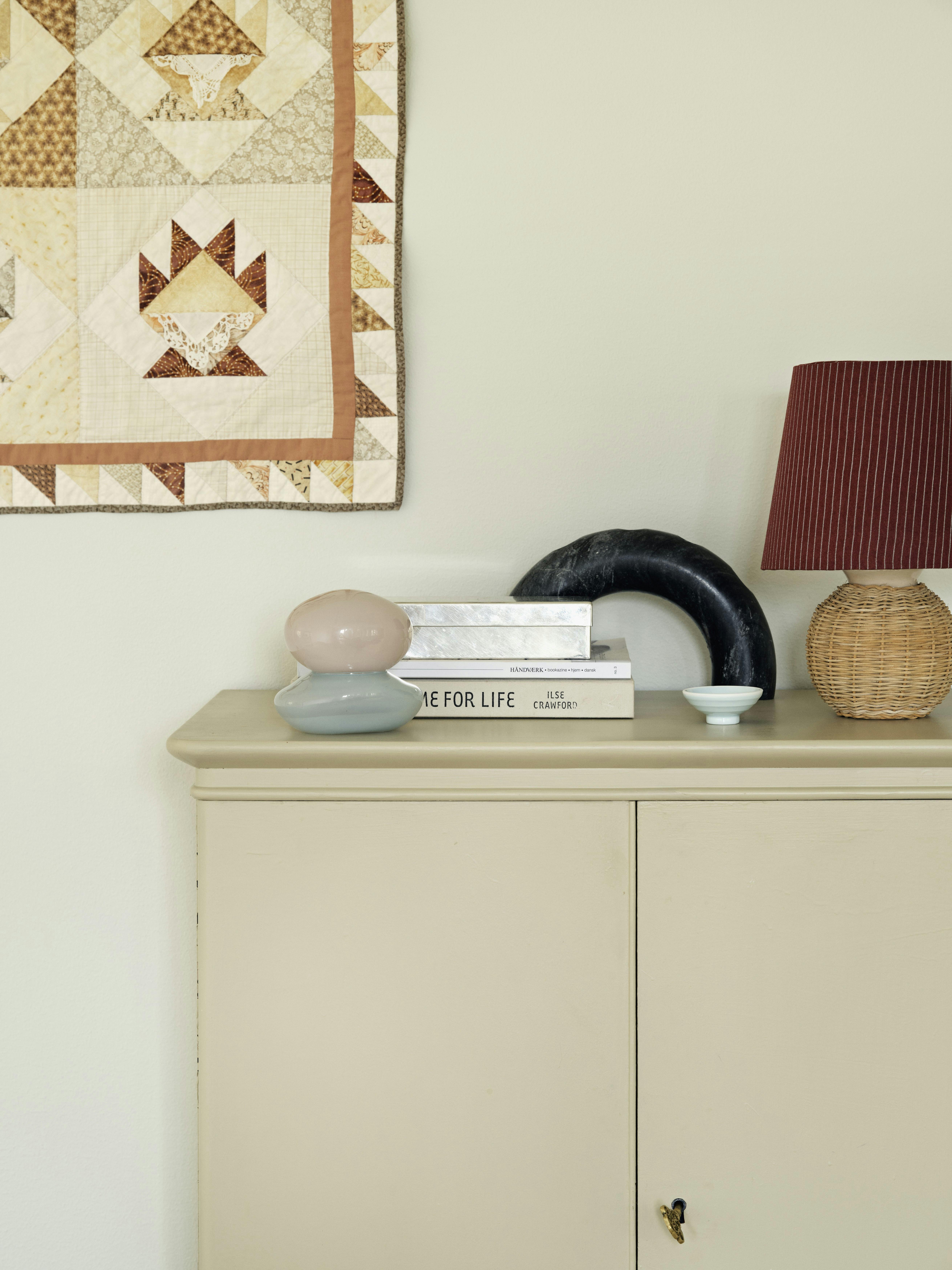 Bonbonniere fra Helle Mardahl, æske i stål fra Shop Dora, halvmåne i sten fra Ferm Living, fletlampe fra Boho Habits og lampeskærm fra Stilleben. Vægtæppet er vintage.