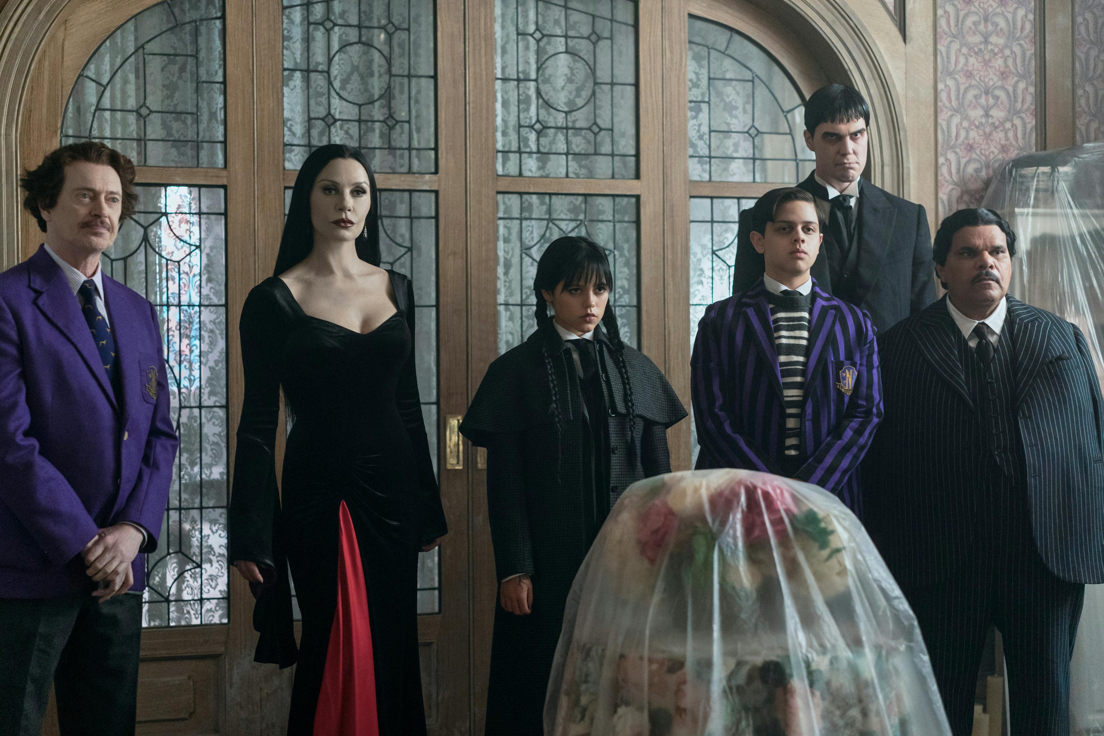 Wednesday. (L to R) Steve Buscemi as Barry Dort, Catherine Zeta-Jones as Morticia Addams, Jenna Ortega as Wednesday Addams, Isaac Ordonez as Pugsley Addams, Joonas Suotamo as Lurch, Luis Guzmán as Gomez Addams in episode 201 of Wednesday. Cr. Jonathan Hession/Netflix © 2025