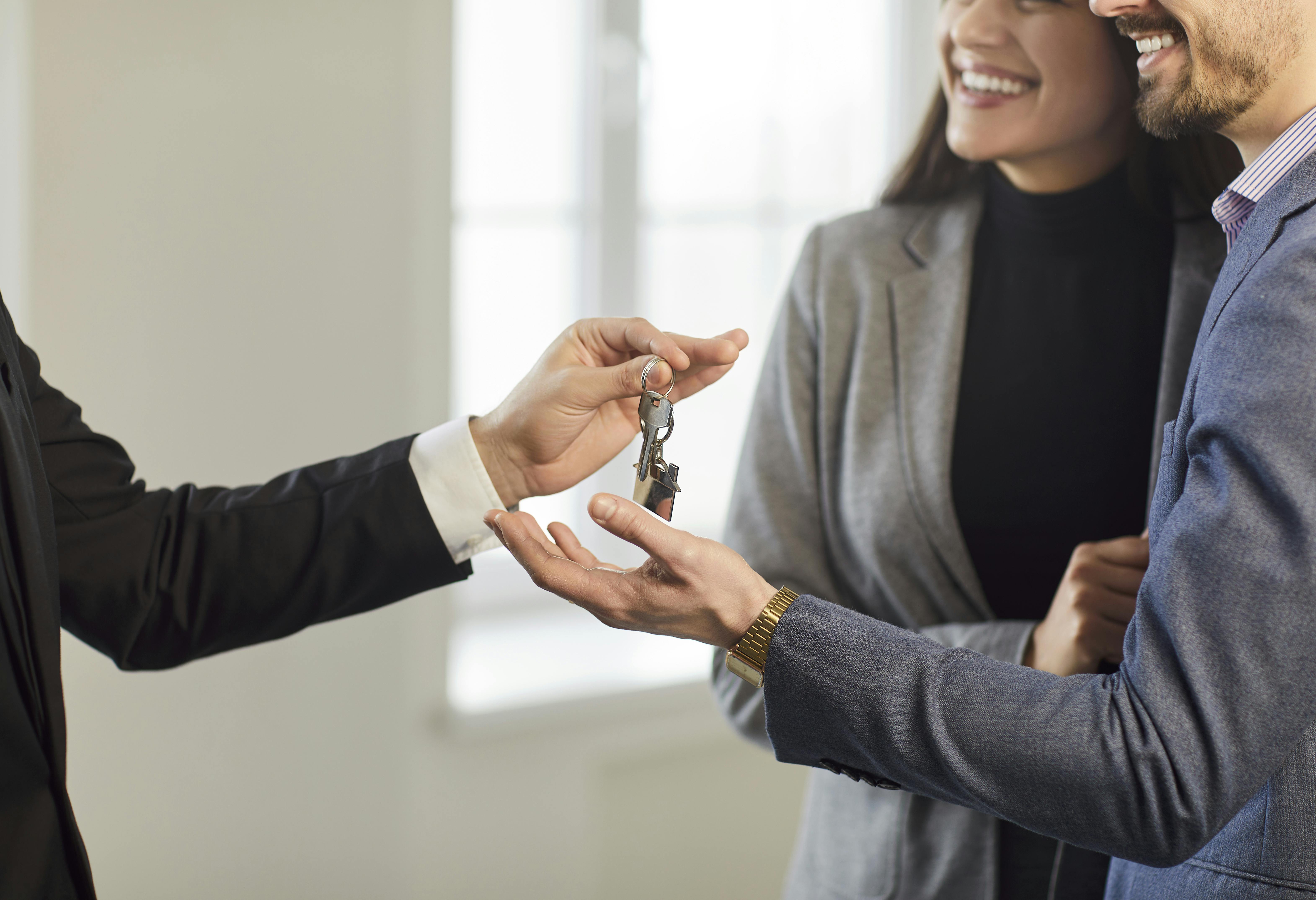 Close-up of family couple receives keys to new home from real estate agent or realtor, celebrating purchase agreement, joyful handover in a home setting marked by successful property acquisition.