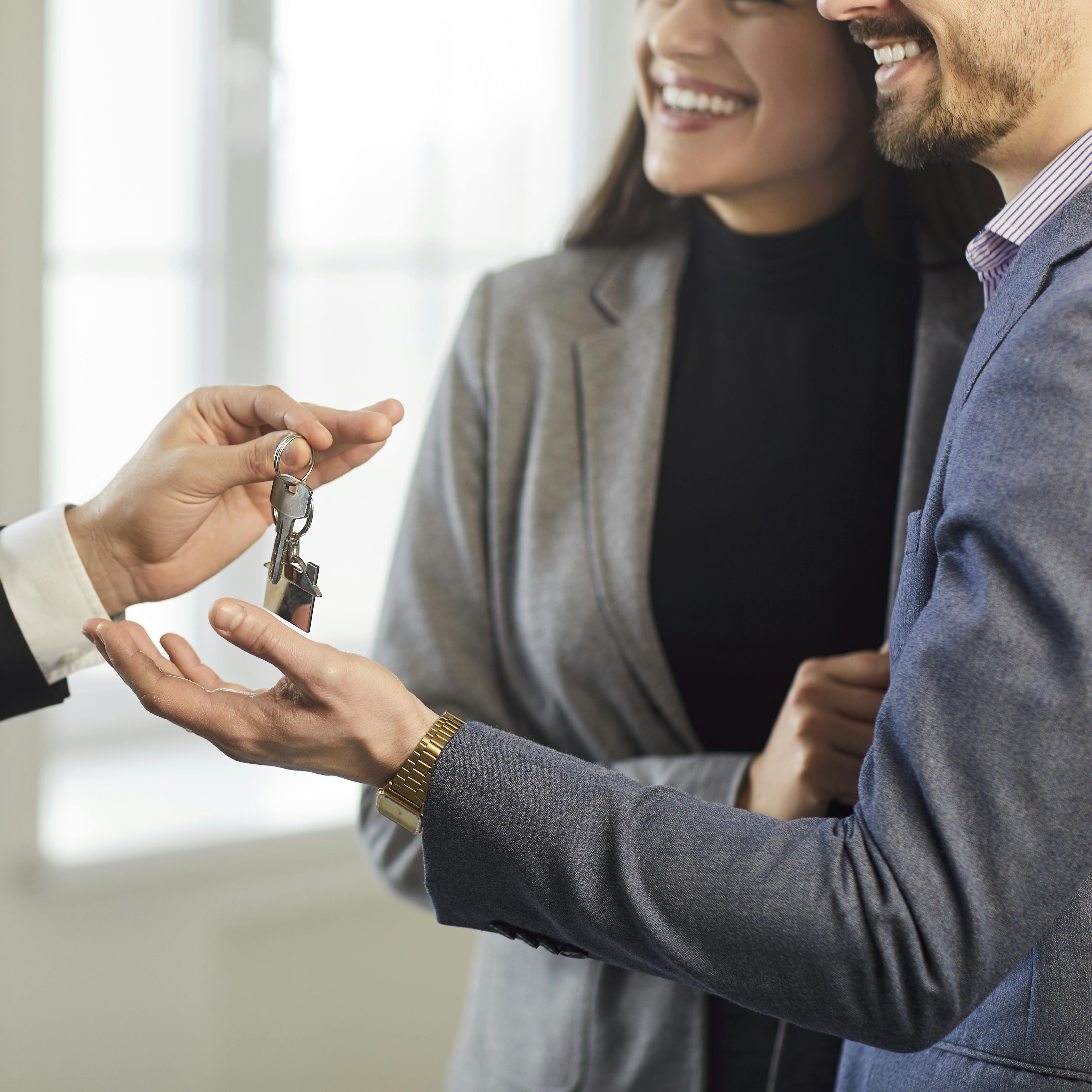 Close-up of family couple receives keys to new home from real estate agent or realtor, celebrating purchase agreement, joyful handover in a home setting marked by successful property acquisition.