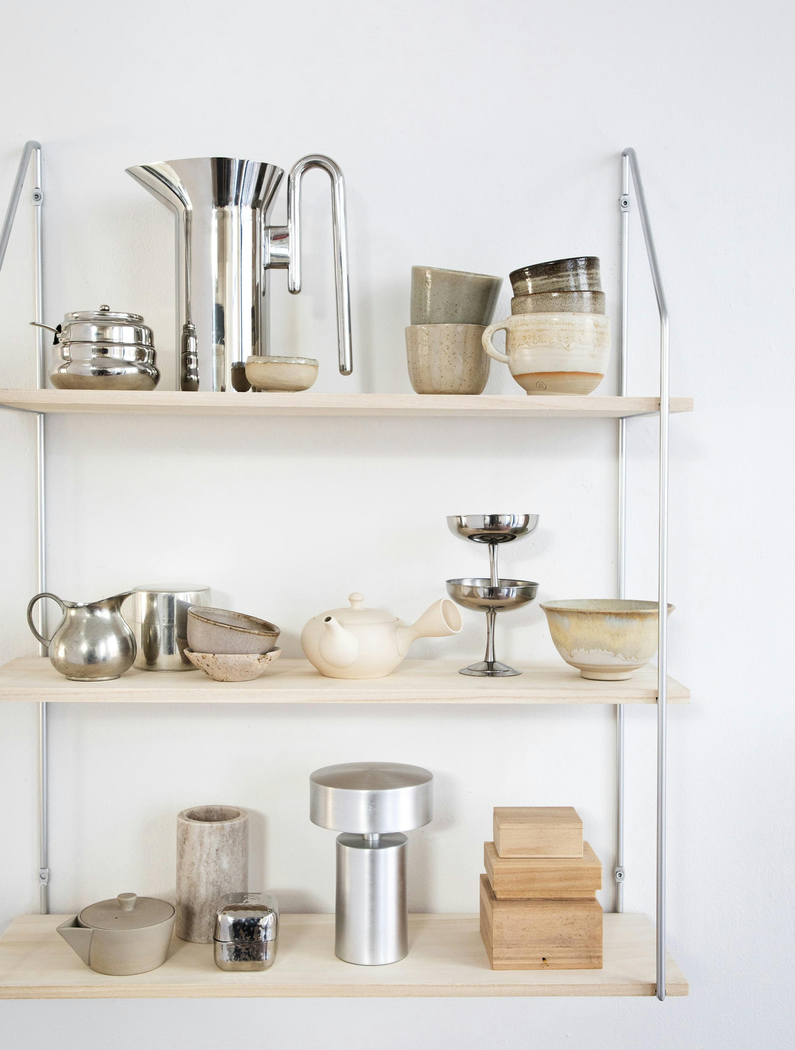Hylder og ophæng fra Jysk, spraymaling fra Panduro Hobby, sukkerskål med låg, lille vintageflødekande og dåse i tin fra Dora, stålkande fra &Tradition, keramikskål, tekande og små trææsker fra Sakura Copenhagen, stribet krus fra @lersakspapir, LED-lampe fra Audo Copenhagen og stålskåle fra Hay.