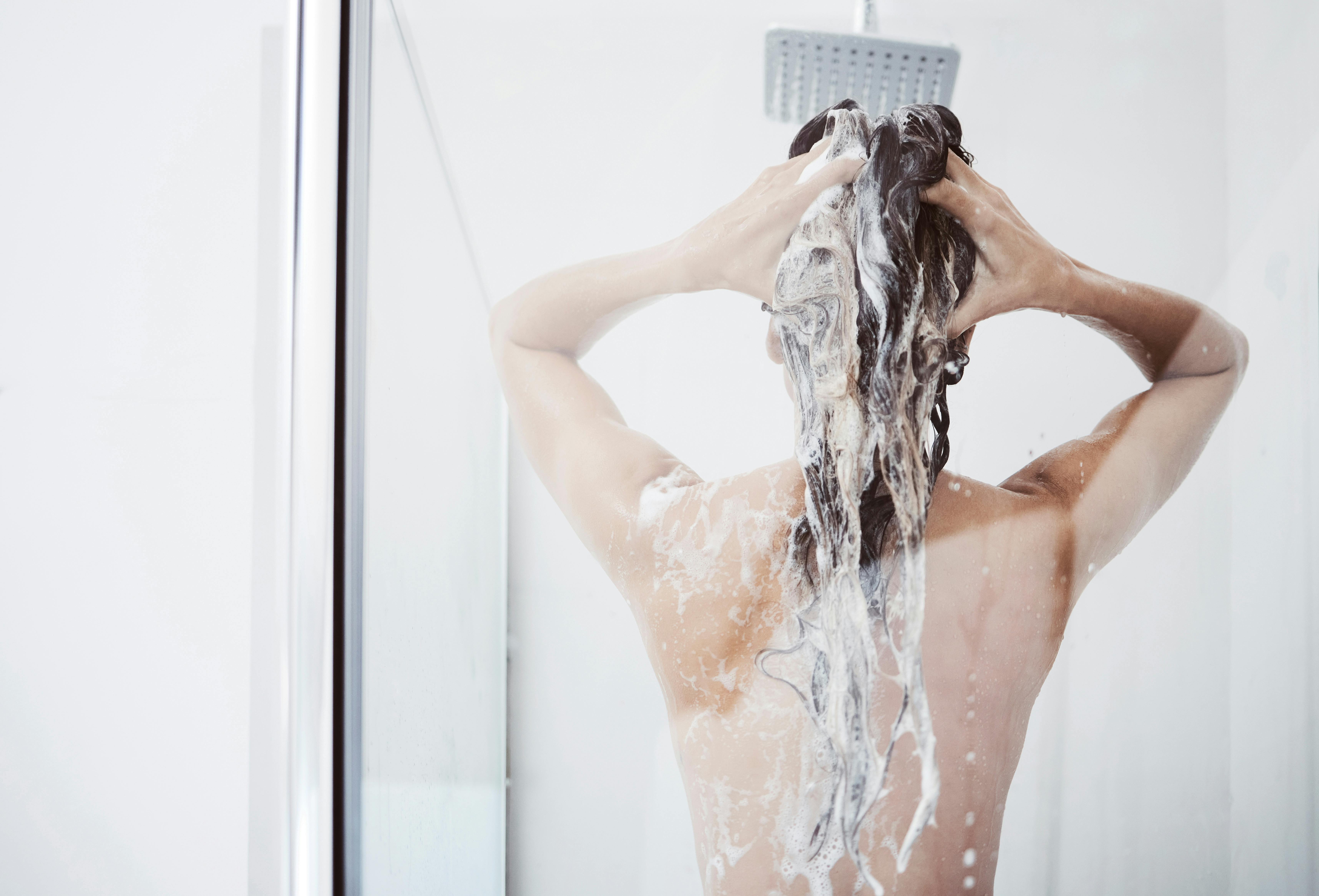 Shower, washing and woman in bathroom with haircare for shampoo, natural treatment or organic cosmetics. Back view, body and female person with foam for hygiene, cleaning or morning routine in home.