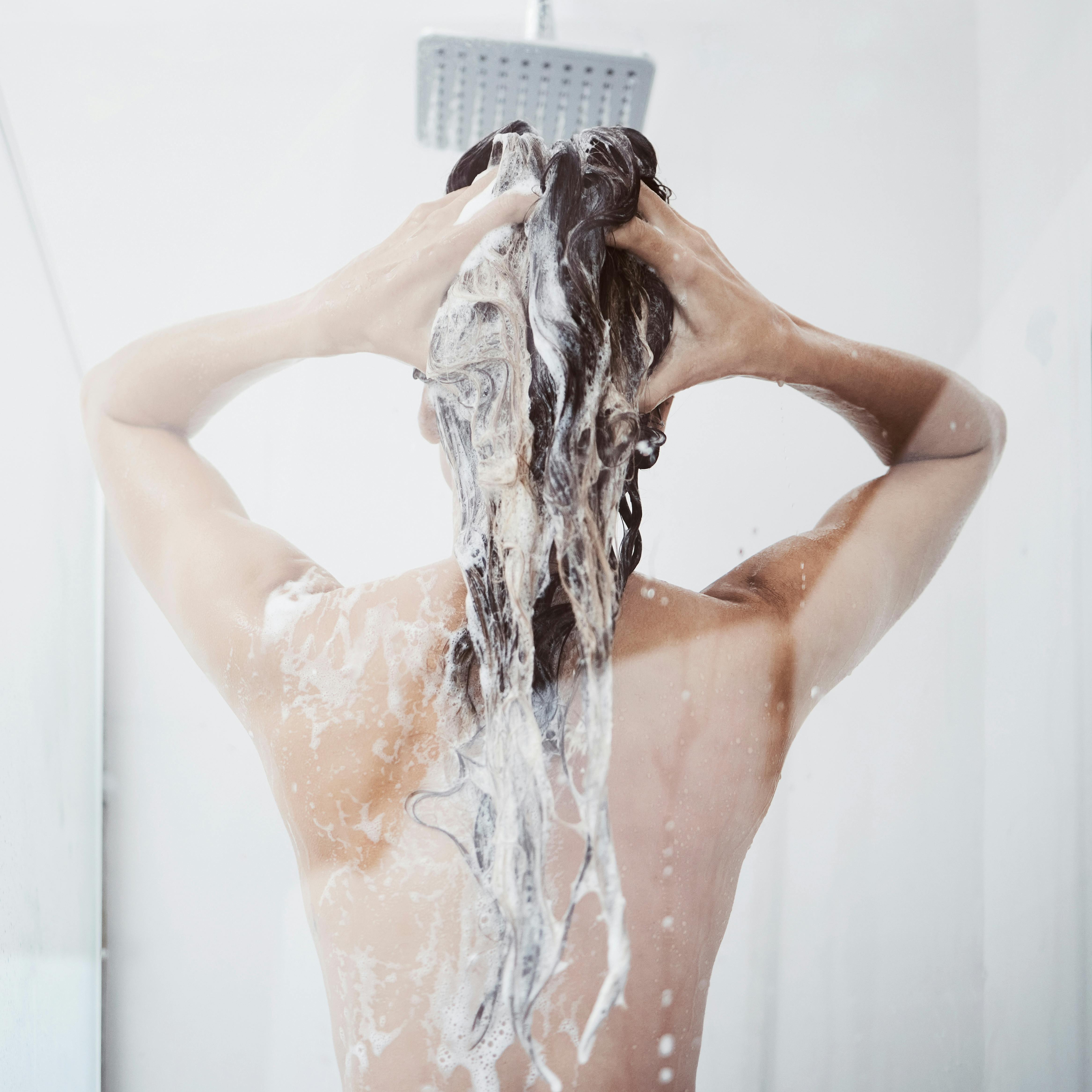 Shower, washing and woman in bathroom with haircare for shampoo, natural treatment or organic cosmetics. Back view, body and female person with foam for hygiene, cleaning or morning routine in home.