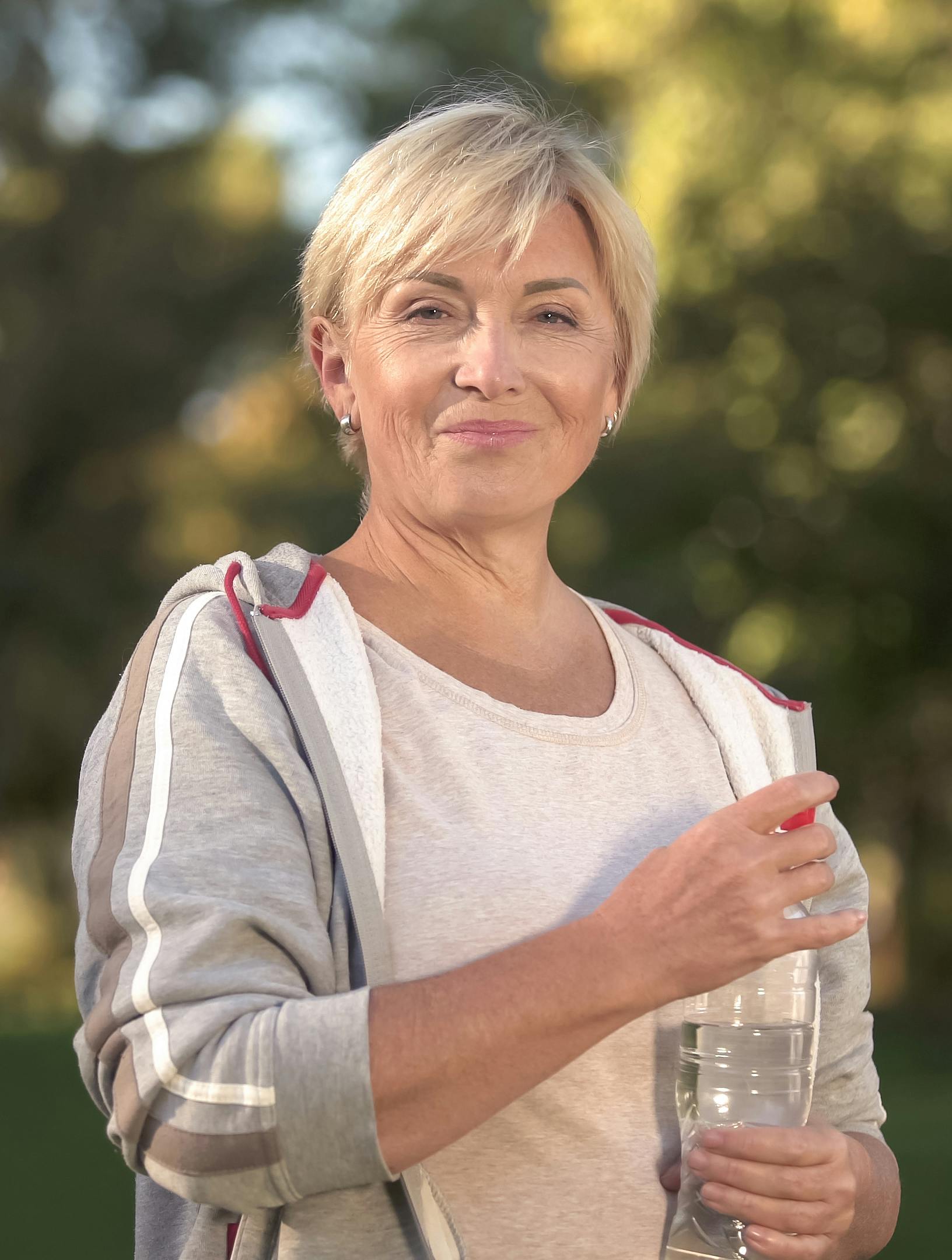 Pretty middle aged woman drinking water in park, keeping water balance, health