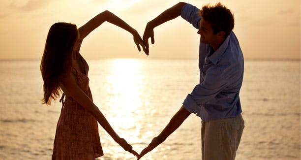 Kærlighed: Mand og kvinde former et hjerte ved en solnedgang over havet