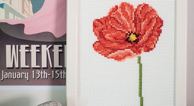 Broderi af korssting med valmue i hvid ramme på bord